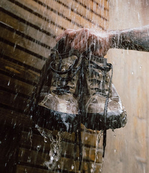 Hand holding Norda trail running shoes under pouring water, highlighting their durability and weather-resistant design.