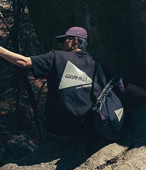 Person exploring outdoors in a Gramicci x And Wander collaboration tee and bag, embodying functional style and adventure.