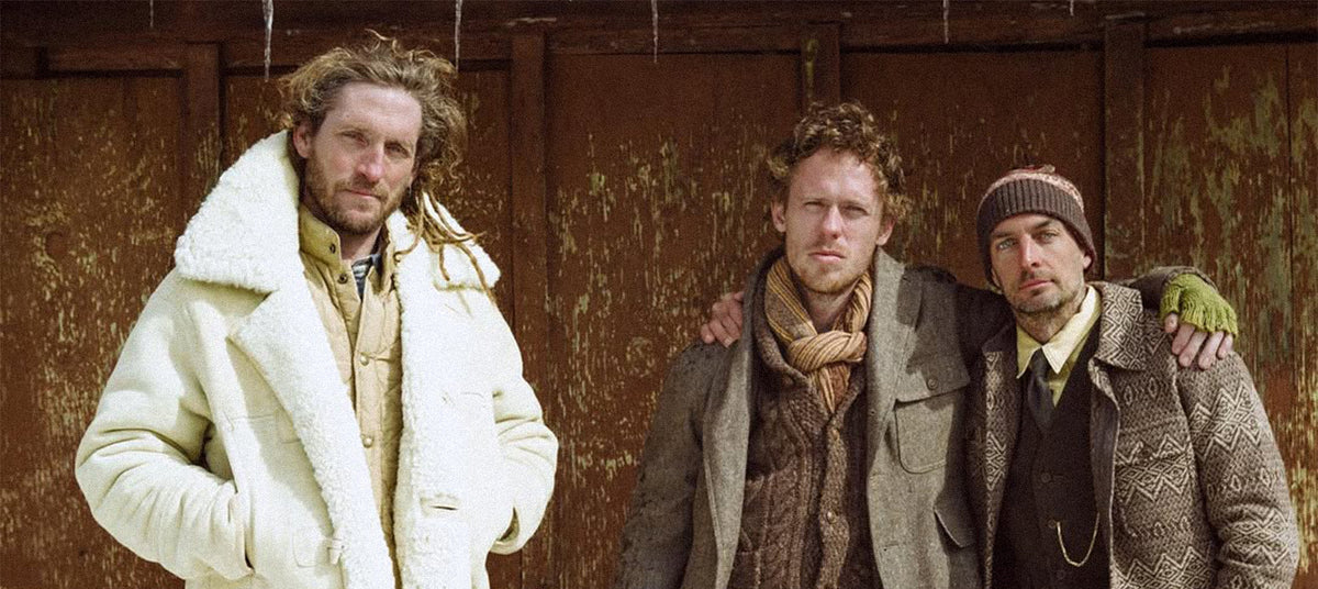 Three men wearing RRL by Ralph Lauren clothing standing together against an old wooden wall.